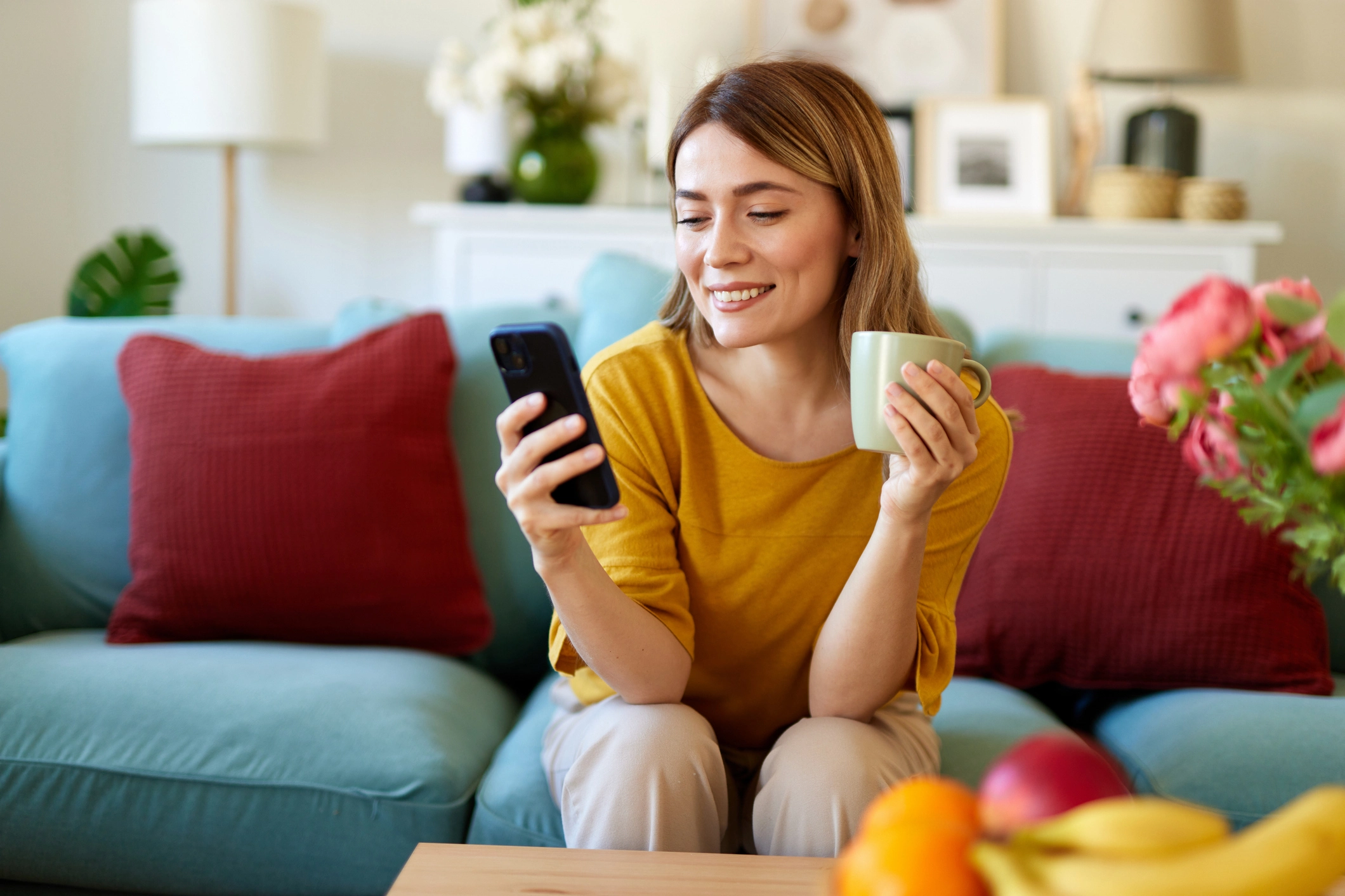 Woman on couch reading phone and holding coffee cup