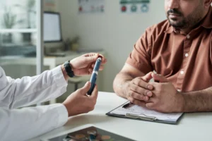 Image of a doctor and a patient in a consultation with no faces showing. Doctor holding a spring-loaded lancing device / Photo d'un médecin et d'un patient en consultation, dont les visages ne sont pas visibles. Le médecin tient un autopiqueur à ressort.